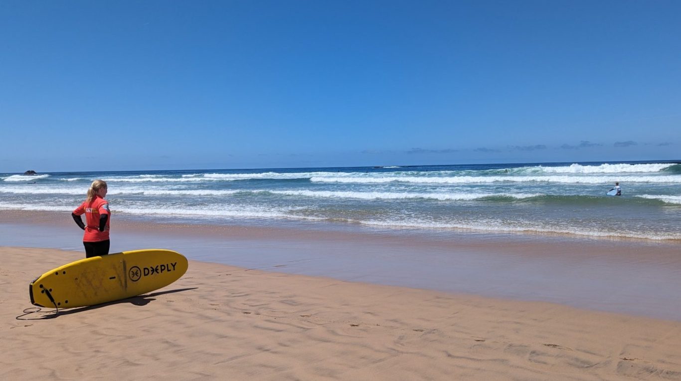 Abenteuerlust © Feb. 2026 Tanja Schöffmann Surferin mit Surfbrett blickt am Strand auf die Wellen hinaus. Ein Symbol für Abenteuerlust