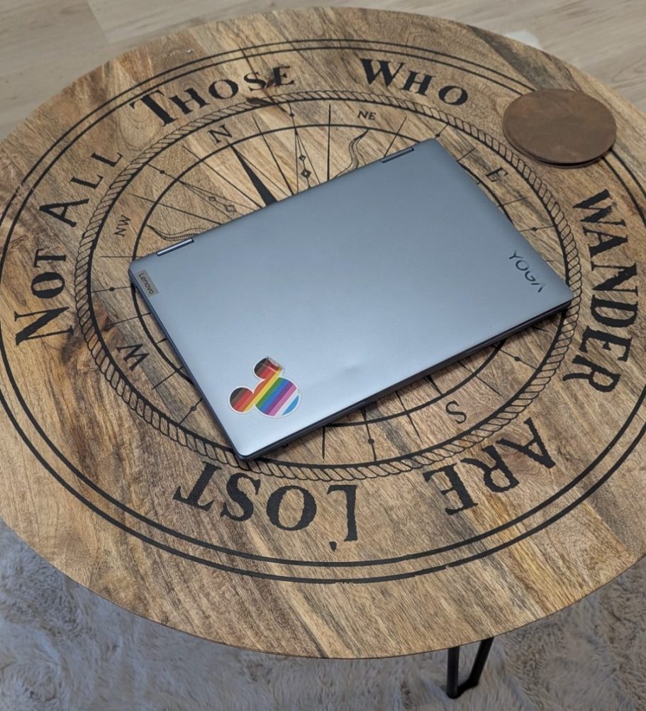 Flexibel online © Feb. 2026 Tanja Schöffmann Grauer zugeklappter Laptop mit Regenbogensticker auf einem braunen, runden Couchtisch auf dem steht "not all those who wander are lost"